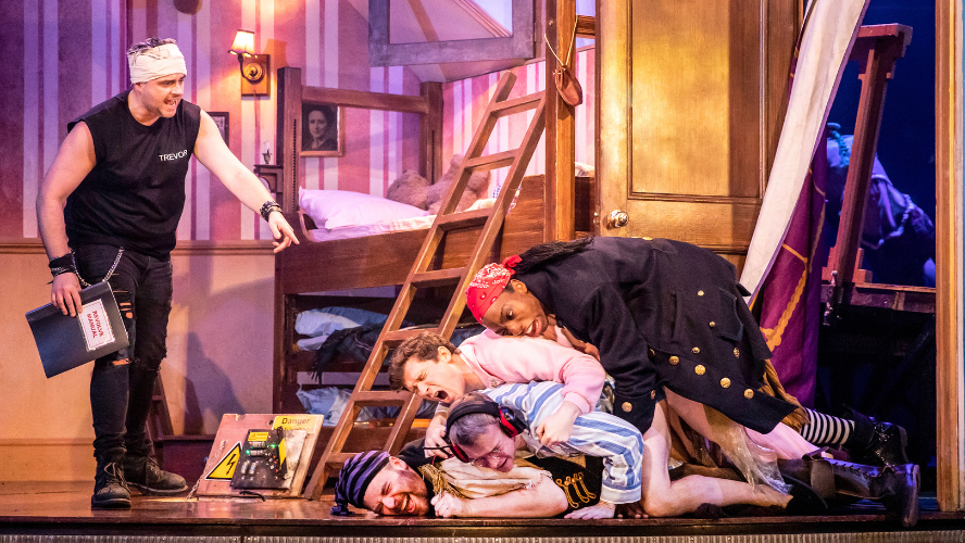 Four men have fallen on top of each other with a stage manager pointing at them.